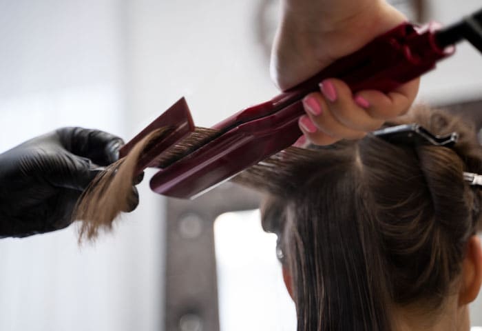 close up de mão vestindo luva de latex preta aplicando chapinha em cabelo castanho escuro